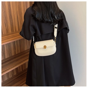 Detail view of cream leather crossbody bag with gold round lock and wide strap on model