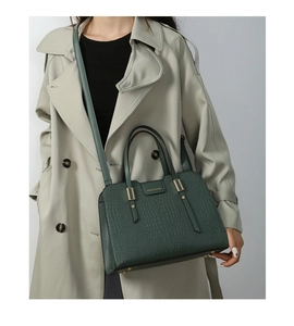 Detailed view of dark green crocodile pattern handbag with gold hardware and logo