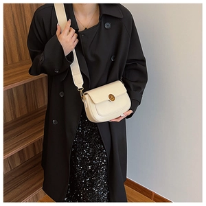 Detail of minimalist beige crossbody bag with round gold buckle on black trench coat