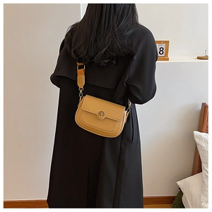 Close-up of khaki leather crossbody bag with metal buckle on black trench coat model