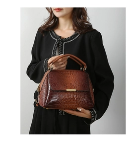 Detail of dark brown crocodile texture handbag with golden metal hardware and round handles