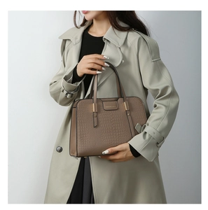 Detail of elegant dark brown crocodile embossed handbag held by model in trench coat