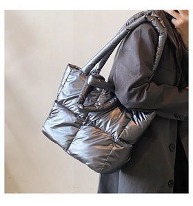 Side view of model wearing a large quilted metallic down tote bag in dark silver grey