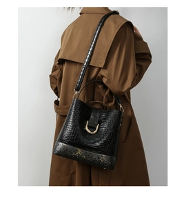 Close-up of black crocodile embossed bucket bag with gold U-shaped buckle on model