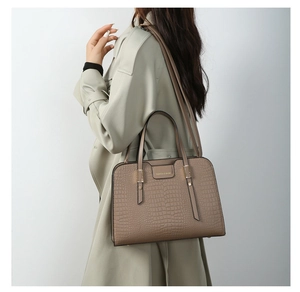 Detail view of a taupe crocodile embossed handbag worn with a light green trench coat
