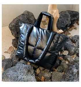 Detail of glossy black quilted down tote bag placed on dark volcanic stones for contrast