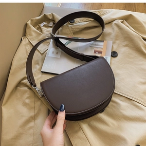 Détail d'un sac selle marron foncé en cuir grainé posé sur un trench-coat beige