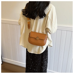 Close-up of brown leather saddle bag featuring a round gold embossed buckle and wide strap