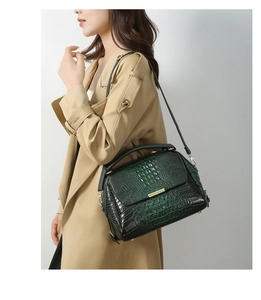 Detail of dark green crocodile texture handbag with gold hardware on khaki trench coat