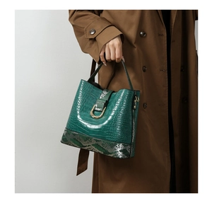 Detail of dark green crocodile pattern bucket bag with golden horseshoe buckle and snakeskin trim