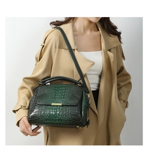 Detail view of dark green crocodile pattern handbag with gold hardware and protective feet