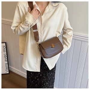 Brown leather saddle bag with wide woven strap shown in a stylish urban lifestyle setting