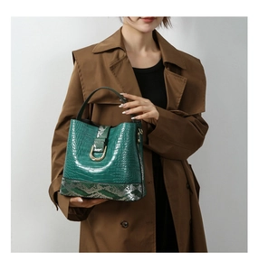 Detail of dark green crocodile texture handbag with snakeskin accents and U-shaped gold buckle
