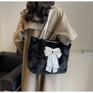 Detailed side view of black plush tote bag with white bow worn with a khaki trench coat