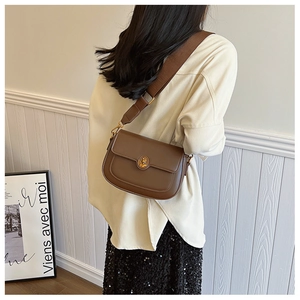 Brown vintage leather crossbody bag featuring a round metal lock and wide fabric strap