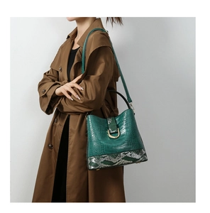 Detail of dark green crocodile pattern bucket bag with snake skin base and gold buckle