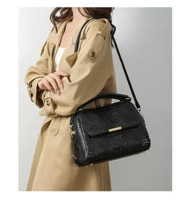 Side view of black crocodile pattern handbag with gold clasp on beige trench coat