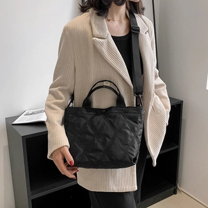 Borsa tote nera trapuntata con tracolla larga indossata da una modella in blazer