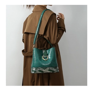 Detail of dark green crocodile texture bucket bag with snake pattern and gold U-buckle