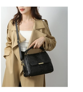 Detail of black crocodile texture handbag with gold metal hardware on trench coat