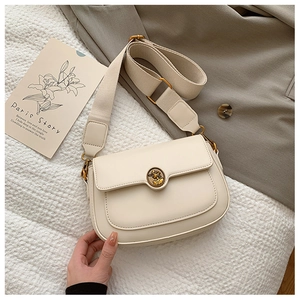 Detail of vintage gold embossed buckle and wide strap on cream-colored crossbody bag