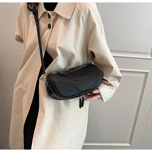 Detail of black cylindrical crossbody bag with vertical pleated texture on beige trench coat