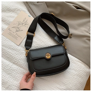 Close-up of black retro shoulder bag with golden emblem and wide woven strap detail