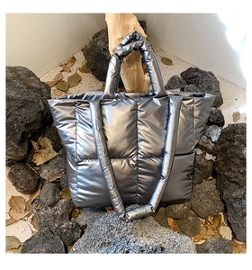 Close-up of metallic silver quilted down tote bag with wide handle on volcanic rock