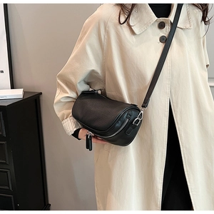 Detail of black textured leather cylinder crossbody bag with silver zipper on beige coat
