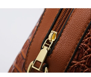 Detail of golden metal zipper on brown crocodile and lychee textured leather bag