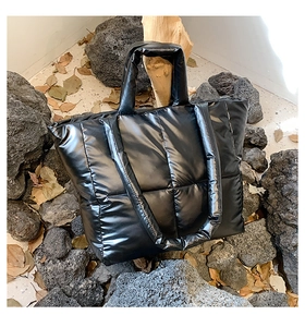 Detail of black glossy quilted tote bag with padded handles on volcanic rocks and leaves