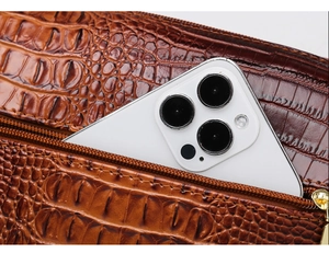 Macro detail of brown crocodile embossed leather handbag with zipper and smartphone inside