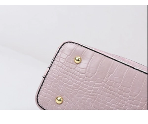 Close-up of pink crocodile pattern shoulder bag with gold metal feet and black edges