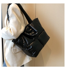 Detail of a large black quilted down tote bag worn on shoulder over a white coat
