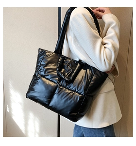 Model wearing a black quilted down tote bag with a shiny finish and wide shoulder strap