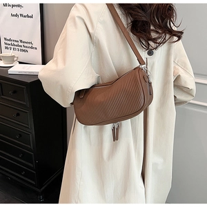 Detailed view of brown cylindrical shoulder bag with pleated texture and tassel zipper