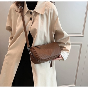 Detail of a brown pleated leather cylinder crossbody bag worn with a beige trench coat
