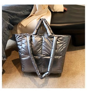 Detail shot of silver quilted puffer tote bag on carpet showing metallic texture and strap