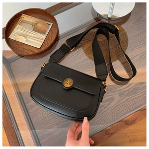 Detail of black leather crossbody bag featuring round gold embossed crest on a wide strap