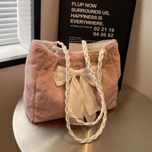 Pink faux fur tote bag with a white tulle bow and woven straps on a metal desk