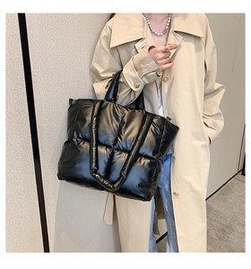 Detail of black quilted puffer tote bag with glossy finish on a khaki trench coat