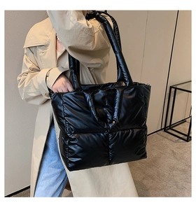 Detail of a large black padded tote bag with diamond quilting and wide shoulder strap
