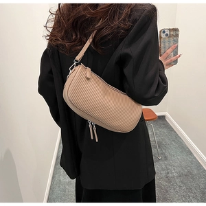 Detail of beige pleated shoulder bag on black blazer showing texture and zip design