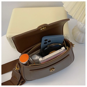 Spacious interior of dark brown leather crossbody bag with phone and makeup items