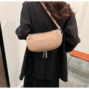 Detail of beige pleated crescent bag on model showing texture and adjustable strap