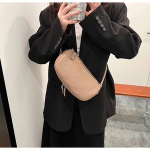 Beige pleated crossbody bag worn by a model in a black blazer for a modern style