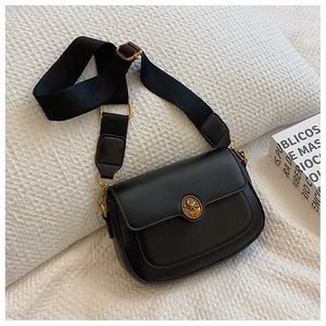 Detail of black leather crossbody bag featuring vintage gold medallion and wide strap