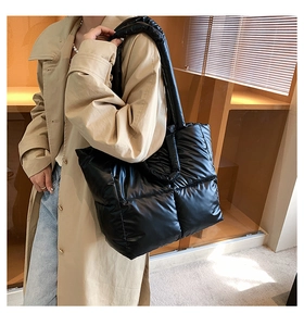 Detail of glossy black quilted tote bag with wide shoulder straps in a home setting