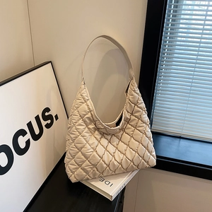 Beige quilted crescent shoulder bag with modern cloud texture and wide strap on desk