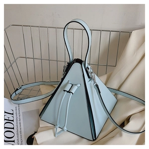 Détail d'un sac pyramide bleu clair sur tissu blanc avec magazine et panier en métal